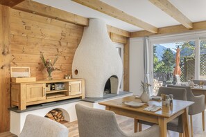 Un intérieur chaleureux avec un mur en bois, une cheminée, un coin repas et une vue sur l’extérieur.