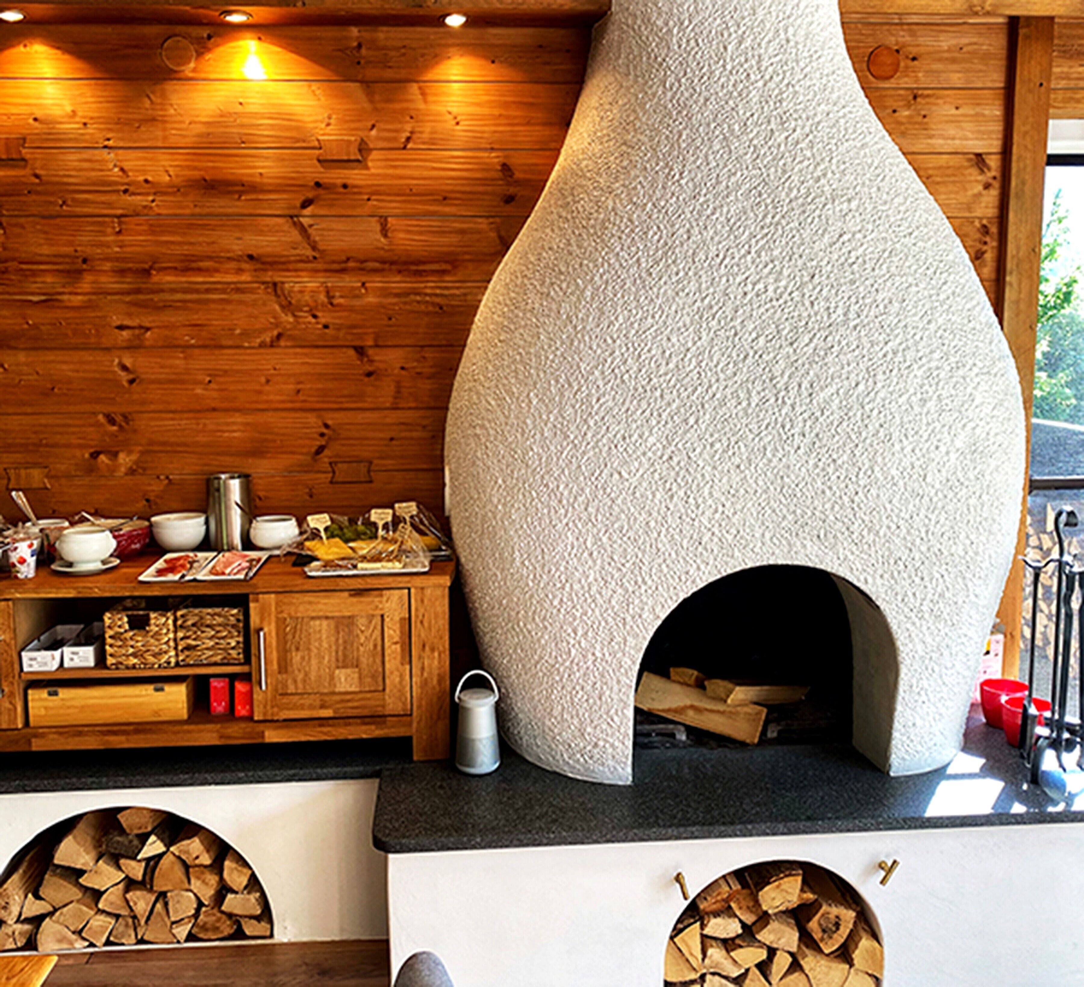 A rustic kitchen with a stone oven, wooden cabinets, and a log storage area.