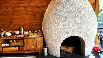 A rustic kitchen with a stone oven, wooden cabinets, and a log storage area.