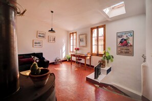 Ein Zimmer mit Schreibtisch aus Holz, einem Sessel, einer Topfpflanze, einem Kaktus und einem Bild an der Wand.