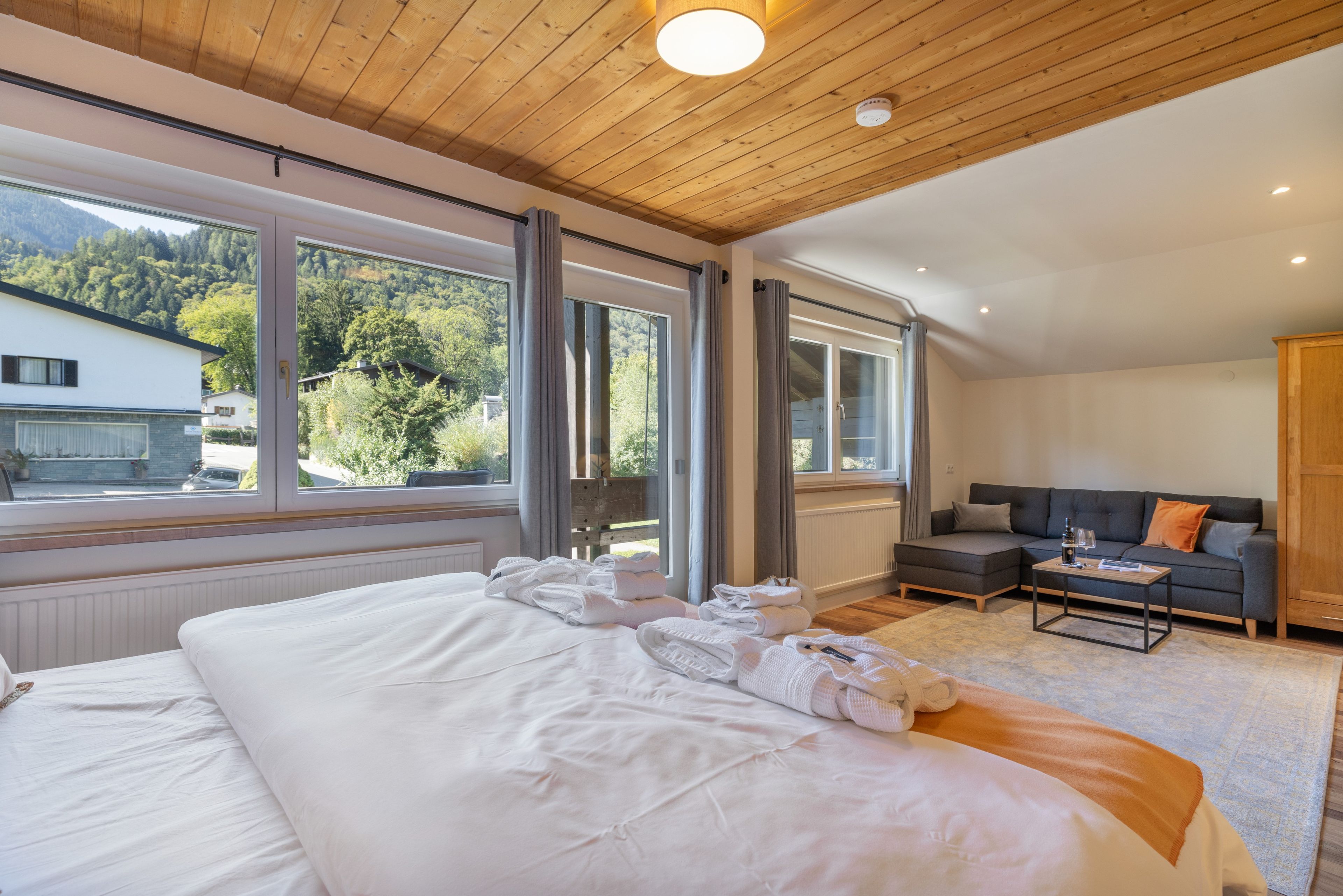 A hotel room with a large bed, a sofa, a coffee table, and a view of the outdoors.