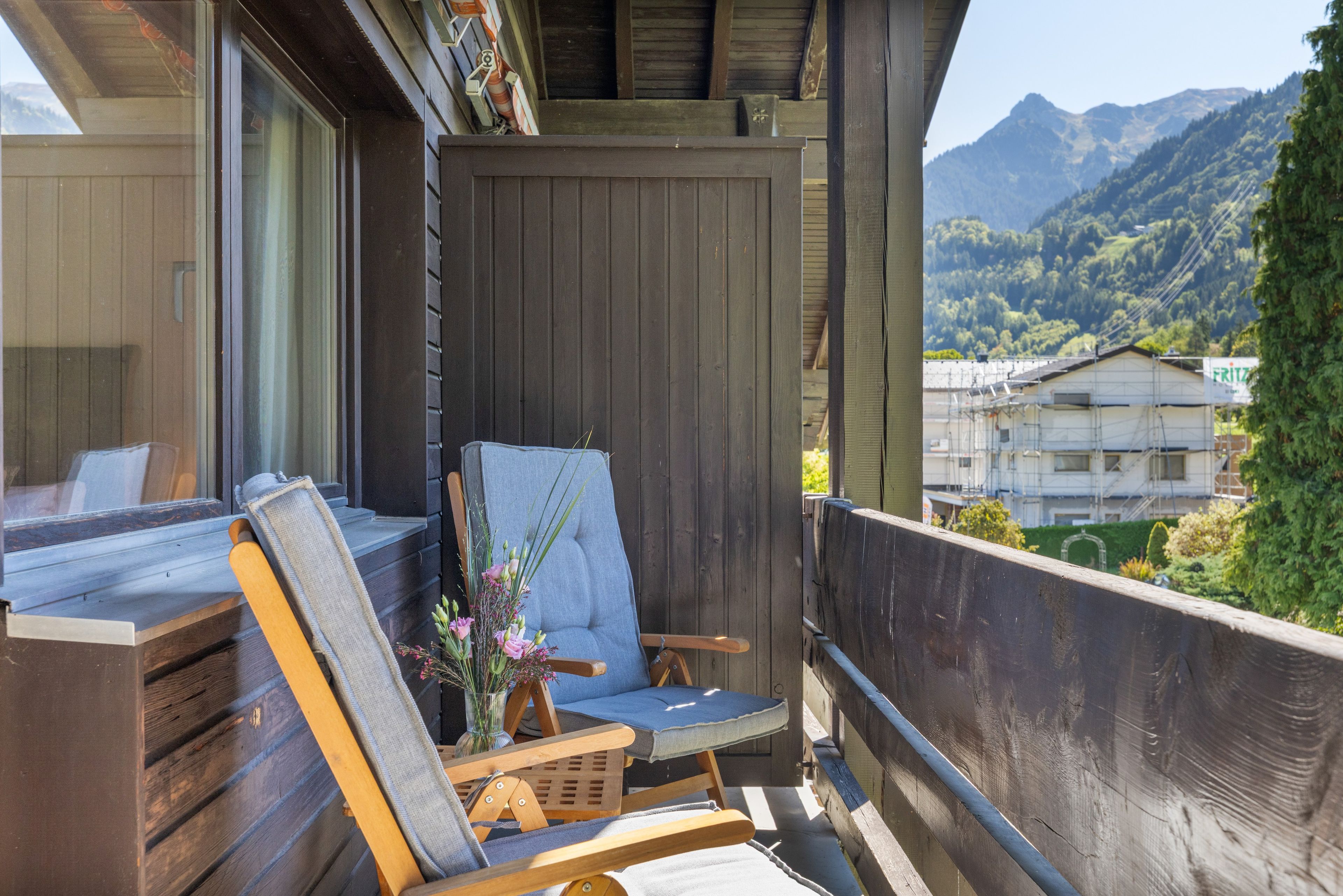 Ein Balkon mit einem Holzstuhl und gepolstertem Sitz, mit Blick auf eine Berglandschaft.