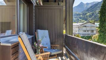 Ein Balkon mit einem Holzstuhl und gepolstertem Sitz, mit Blick auf eine Berglandschaft.