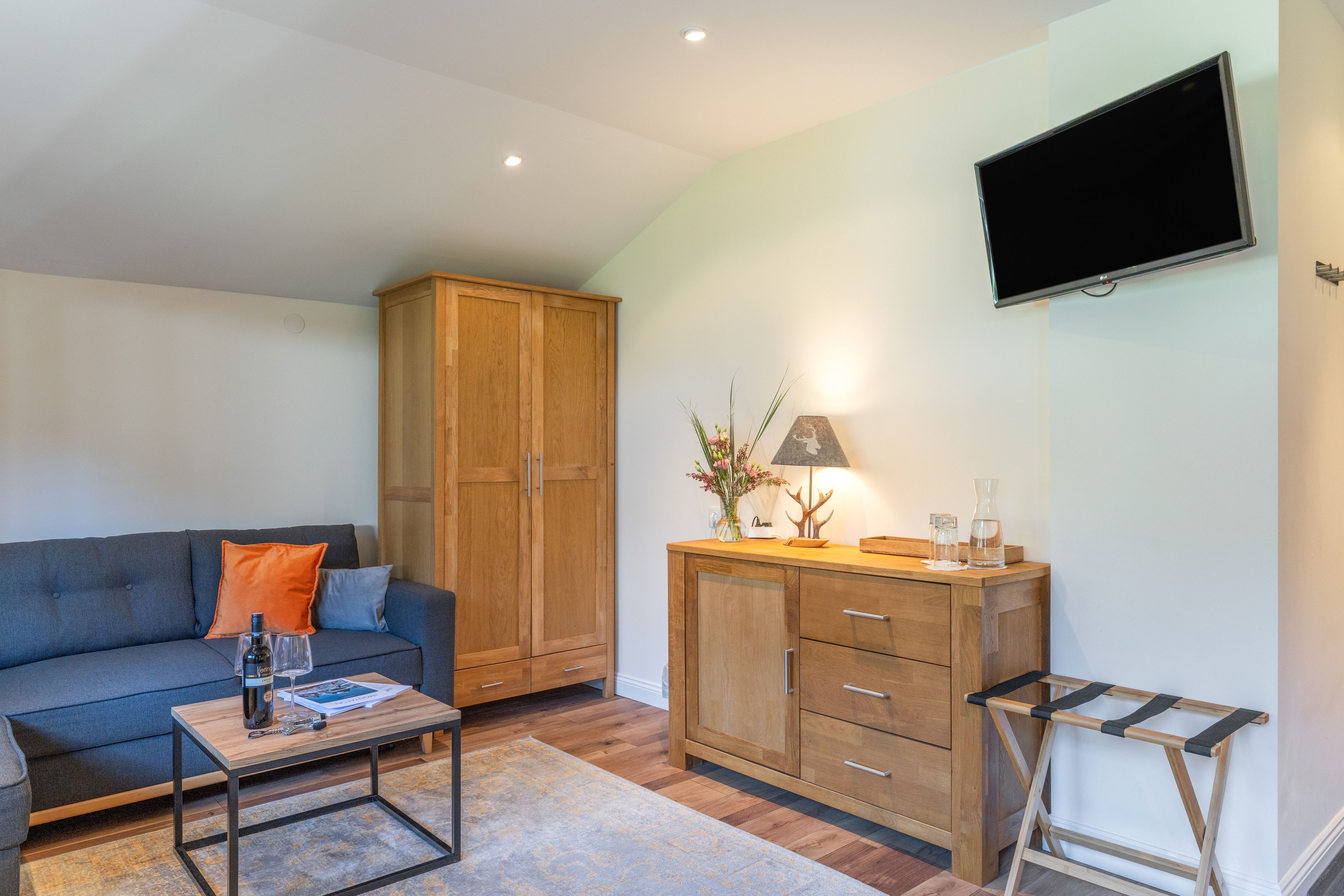 Een woonkamer met een bank, salontafel, houten kast en een aan de muur bevestigde televisie.