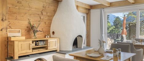 A cozy interior with a wooden wall, a fireplace, a dining area, and a view of the outdoors.