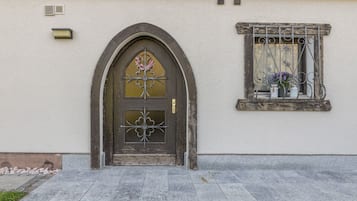A building with a dark wooden door, a window with metal bars, and a small balcony with potted plants.