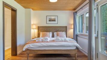 Ein Hotelzimmer mit Holzbalkendecke, einem Bett mit weißen Leinen und Handtüchern, einem gerahmten Bild an der Wand und einem Fenster mit Vorhängen.