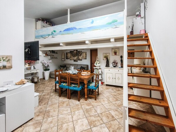 A dining area with a wooden table and chairs, a kitchen with white cabinets, and a staircase leading to an upper level. - Magic DaLu House - Olbia (Olbia)