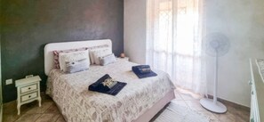 A bedroom with a bed, bedside tables, a floor fan, and a window with curtains. - Magic DaLu House - Olbia (Olbia)
