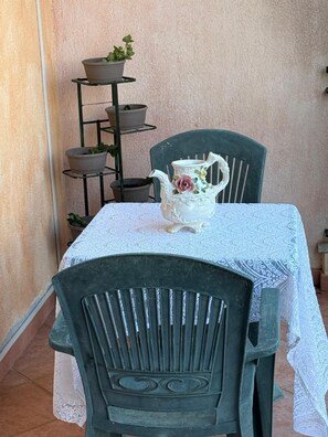A table with a lace tablecloth, a white ceramic pitcher with floral designs, and a green chair. - Charming Apartment in La Maddalena With Private Terrace (Capoterra)