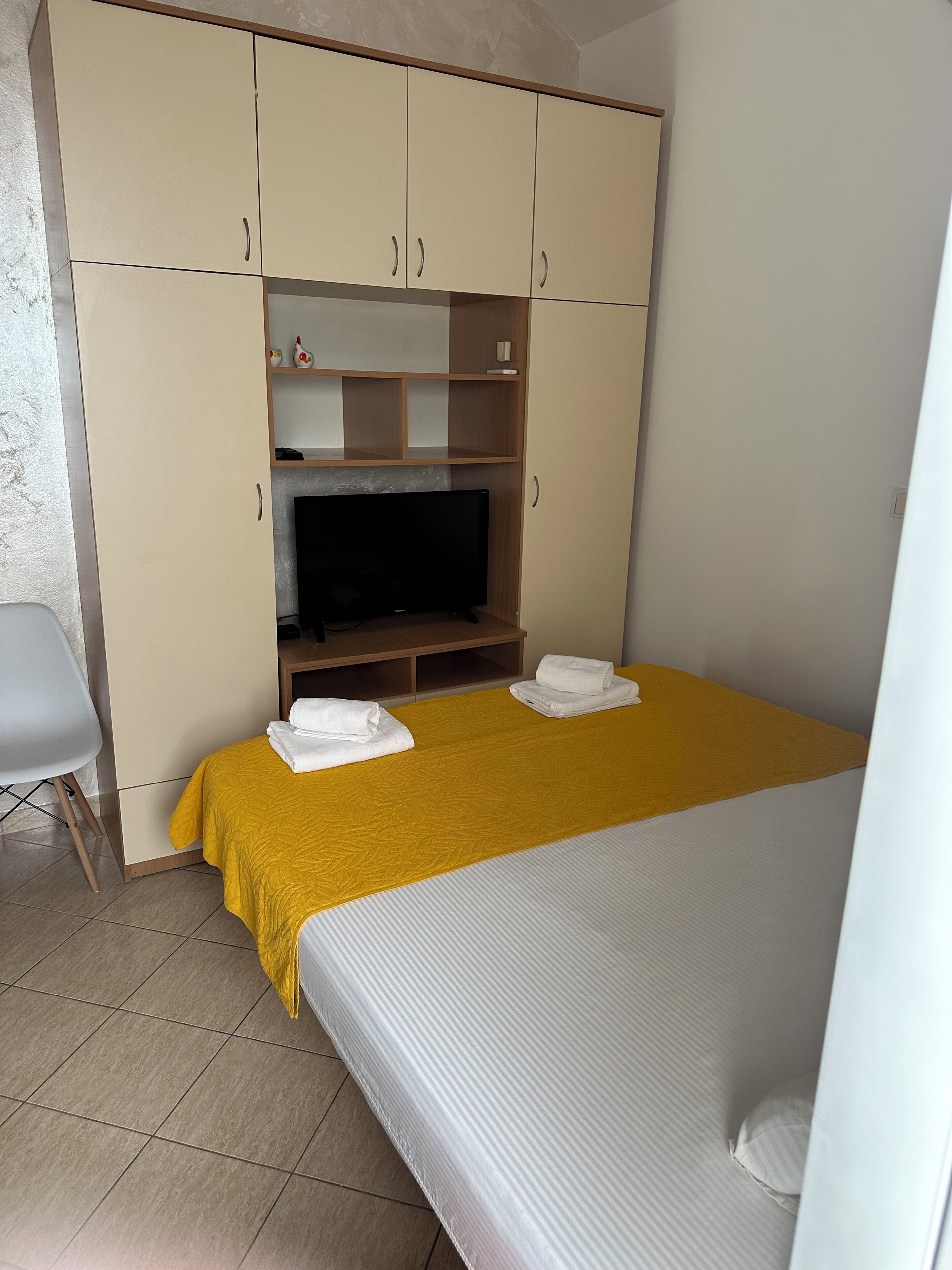 Una habitación de hotel con cama, televisor, armario y una silla.