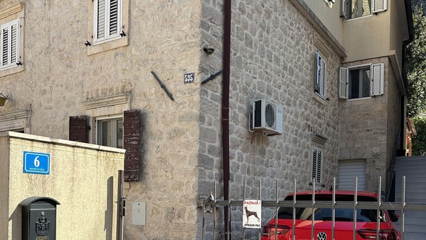A red car parked in front of a building with stone walls and a metal gate. - Studio Apartment Emi Kotor (Kotor)