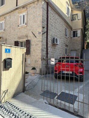 Un coche rojo estacionado frente a un edificio con paredes de piedra y una verja de metal.