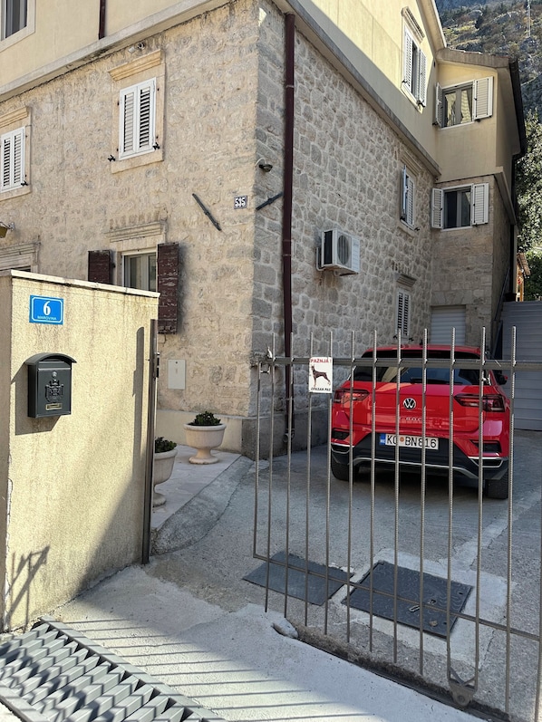 Un'auto rossa parcheggiata di fronte a un edificio con pareti in pietra e un cancello in metallo.
