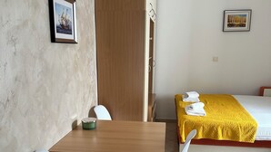 A hotel room with a wooden desk, two white chairs, a bed with a yellow blanket, and a large wardrobe. - Studio Apartment Emi Kotor (Kotor)
