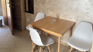 A dining area with a wooden table, two white chairs, a framed picture on the wall, and a cabinet with a built-in refrigerator. - Studio Apartment Emi Kotor (Kotor)