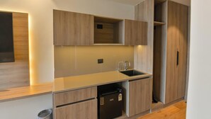 A modern kitchen with wooden cabinetry, a built-in sink, and a compact refrigerator. - Melange Hotel (Gurugram)