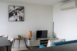 A modern living room with a flat-screen TV, a coffee table, a sofa, and a wall-mounted air conditioner. - Modern high rise apt, with balcony, secure parking (Southbank)
