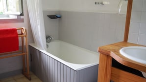 Et badeværelse med et badekar, en træstol med et rødt håndklæde, en hvid vask og et spejl.