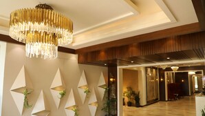 Um lobby moderno com um candelabro, design geométrico na parede e plantas em vasos.