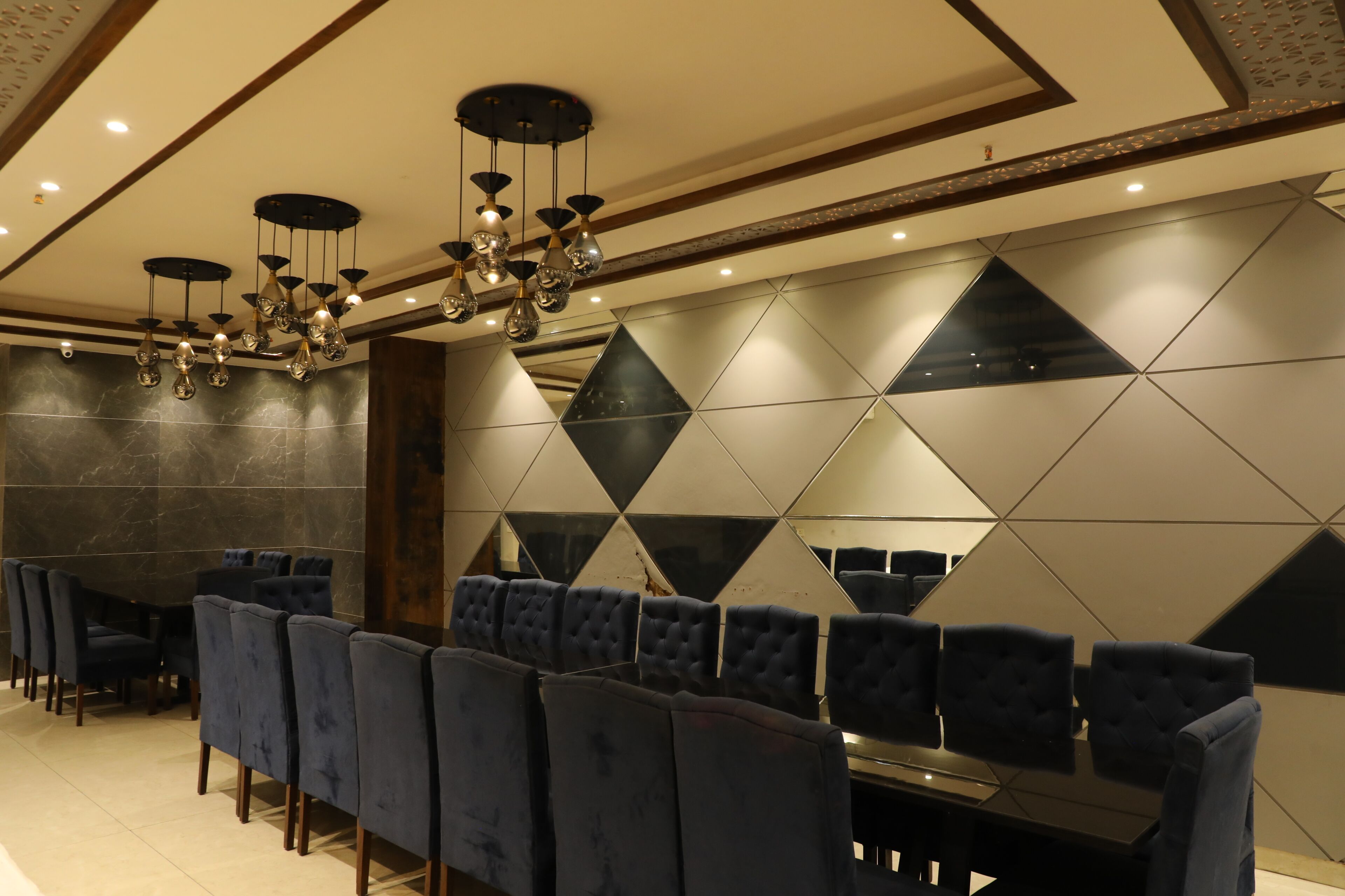 Un interior moderno con una fila larga de sillas tapizadas en azul oscuro, una mesa de comedor central y una pared con estampado geométrico.