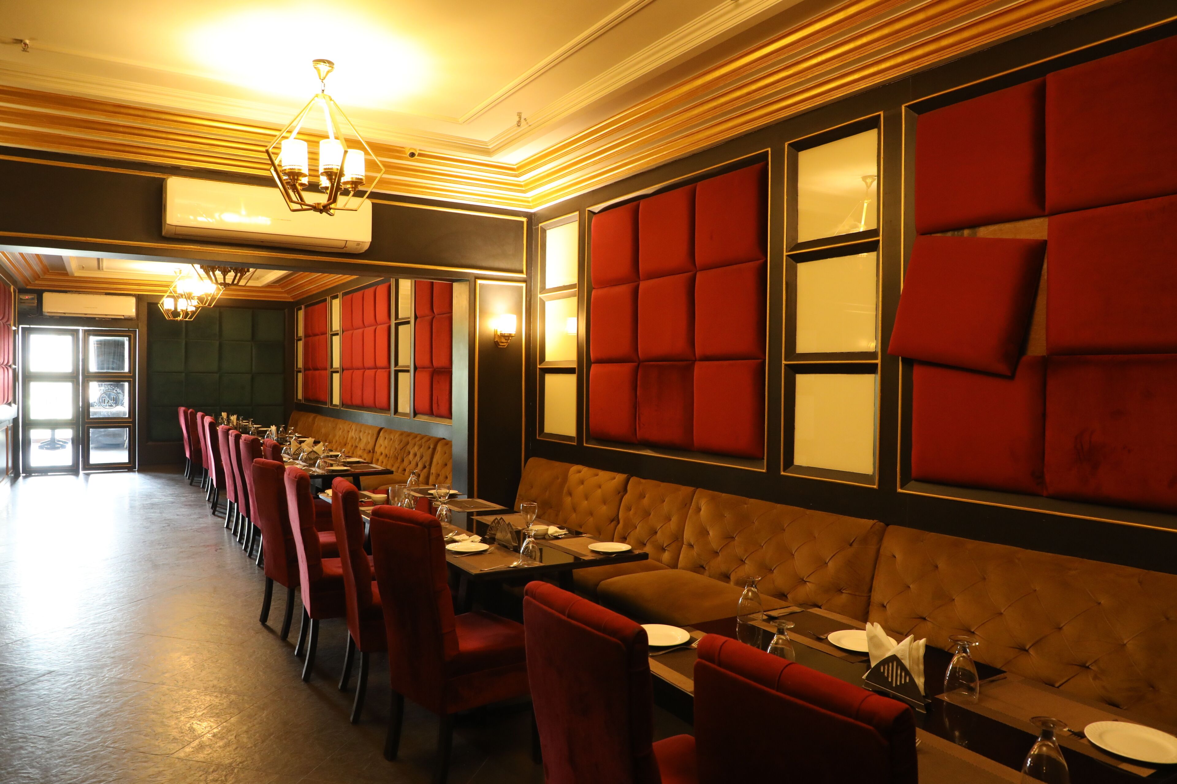 A restaurant with a long counter, red upholstered booths, and a chandelier.