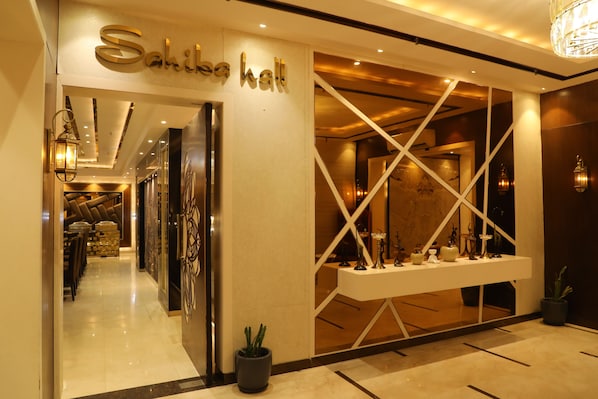 A hotel entrance with a reception desk, a chandelier, and a potted plant.