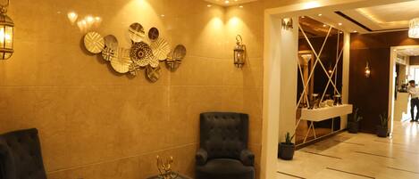 A lobby with two black armchairs, a small black table with a candelabra, decorative wall art, and a chandelier.