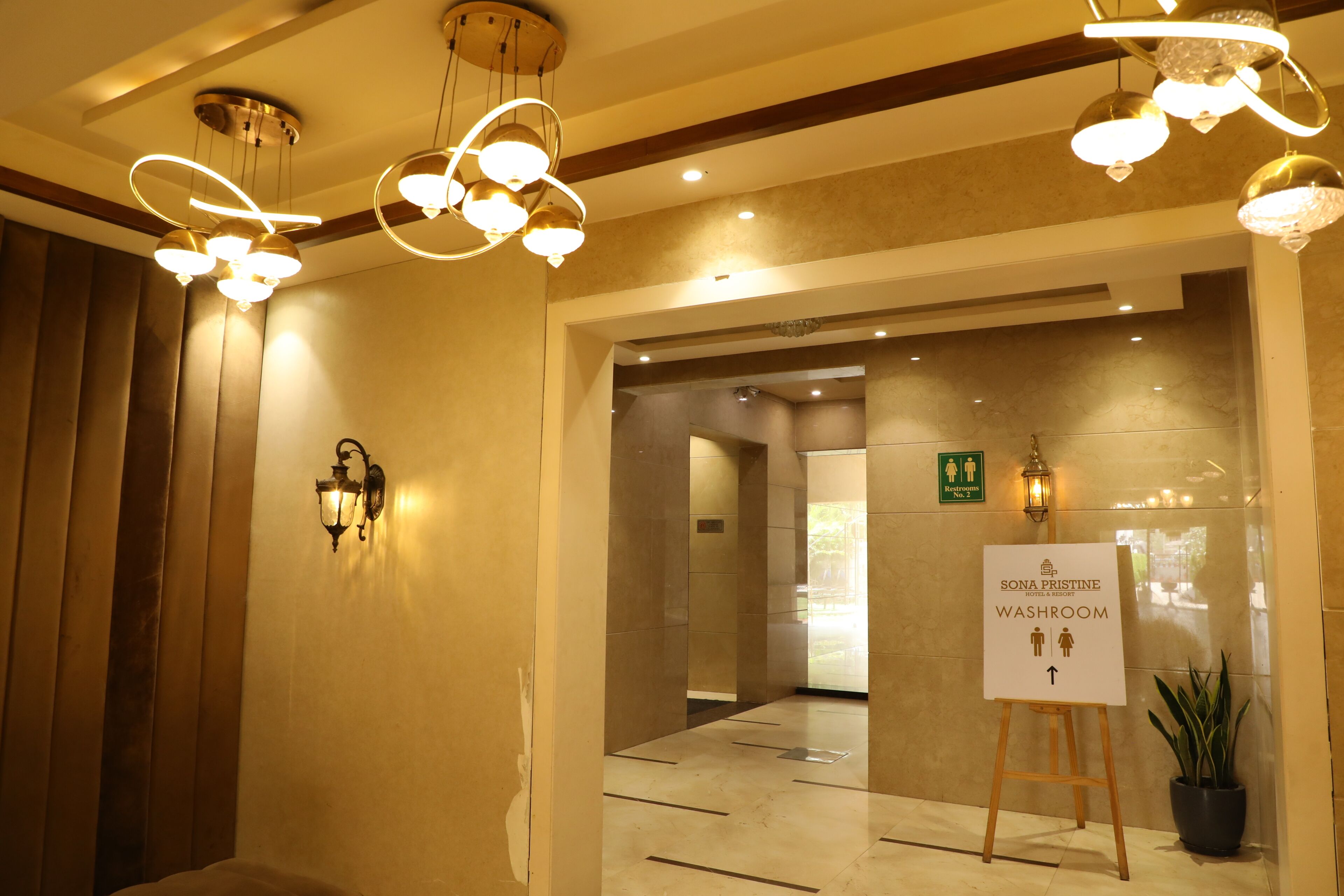 A hotel lobby with a sign indicating a washroom, a potted plant, and a modern light fixture.