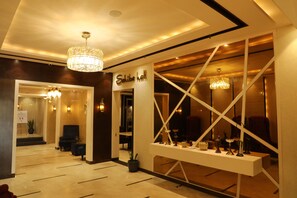 A hotel lobby with a reception desk, seating area, chandeliers, and a display of decorative items.