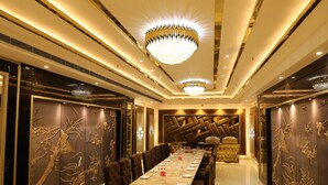 Uma longa mesa de jantar com cadeiras, um lustre e painéis decorativos na parede.