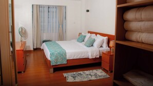 Un dormitorio con cama de madera, una mesita de noche, lámpara de pie, ventilador y una ventana con cortinas.