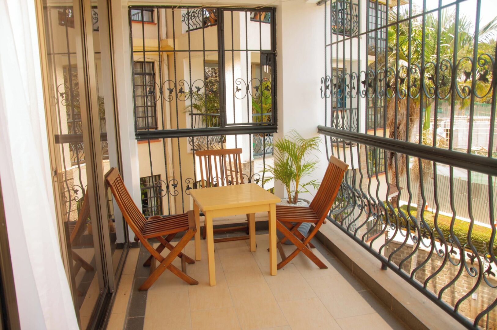 Ein Balkon mit Holztisch und -stühlen, einem Blumentopf und einem dekorativen Metallgeländer.