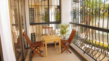 Ein Balkon mit Holztisch und -stühlen, einem Blumentopf und einem dekorativen Metallgeländer.
