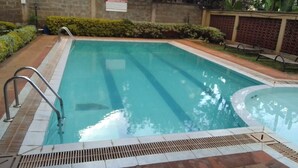 Una piscina rectangular con una escalera metálica en un lateral, rodeada por un solárium con baldosas y setos bajos.