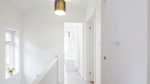 Un couloir aux murs blancs, avec une rambarde blanche et un luminaire suspendu.