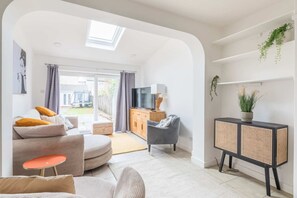 Un salon moderne avec un canapé, un pouf et une petite table. On y trouve également un téléviseur, un meuble et une fenêtre avec des rideaux.