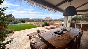 Um pátio com chão de pedra, móveis de madeira e vista para uma piscina e paisagem.