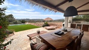 A patio with a stone floor, wooden furniture, and a view of a pool and landscape. - SERENITY POOL VILLA IBIZA (Santa Eulària des Riu)