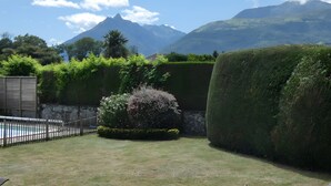 A well-maintained garden with a pool, neatly trimmed hedges, and a mountainous backdrop.