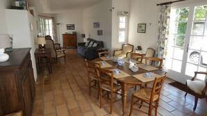 A spacious living area with a dining table set for four, a sofa, and a kitchen area with a refrigerator and cabinets.