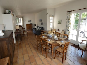 A spacious living area with a dining table set for four, a sofa, and a kitchen area with a refrigerator and cabinets. - Maison l'Oustaou with Pool, Mountain View and Large Enclosed Garden (Ayzac-Ost)