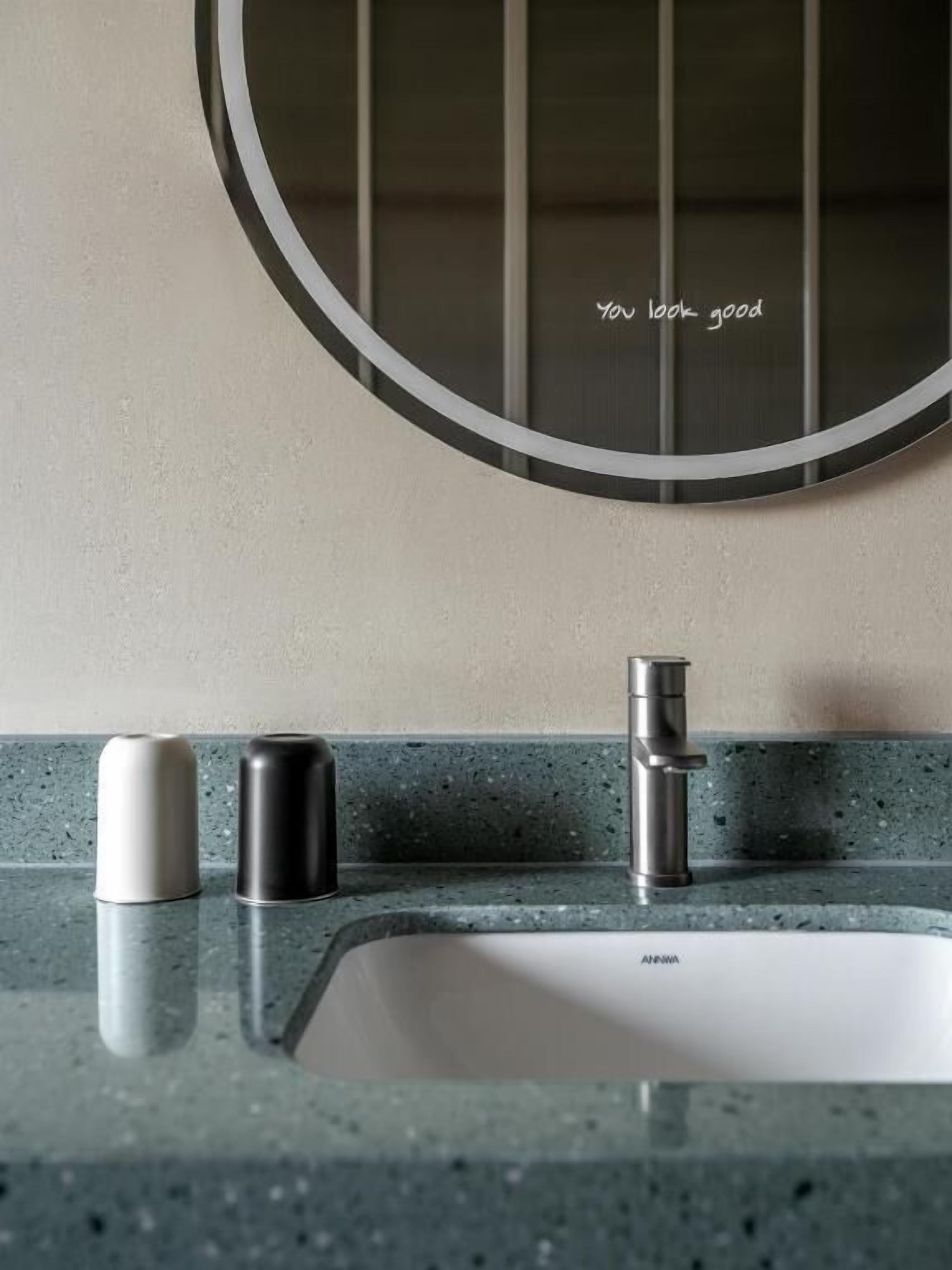 A bathroom with a round mirror, a sink, and two cylindrical containers on the countertop.
