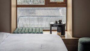 A bedroom with a large window, a bed, a small table, and a green pillow.