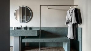 A modern bathroom with a freestanding bench, a round mirror, and a towel rack.