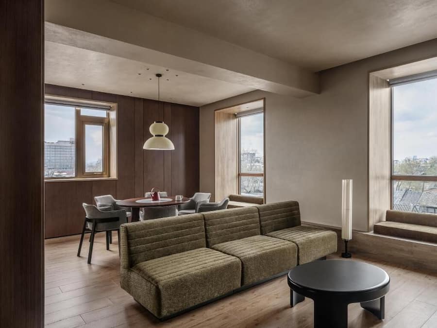 Una sala de estar moderna con sofá, mesa de comedor, sillas y ventanas grandes.