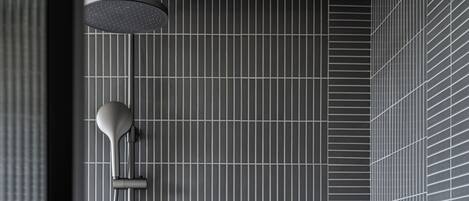 Une douche moderne dotée d’un pommeau de douche à pluie et d’un pommeau de douche à main, d’une étagère murale pour les articles de toilette et d’un mur carrelé avec un motif en réseau.