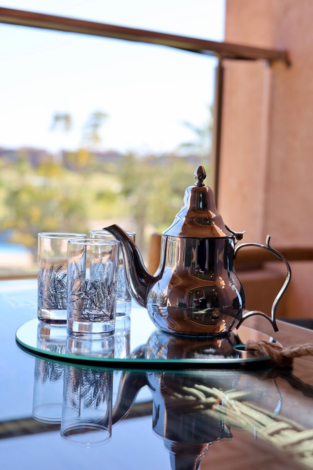 Un juego de té sobre una bandeja de vidrio, con vistas a un paisaje a través de una ventana.