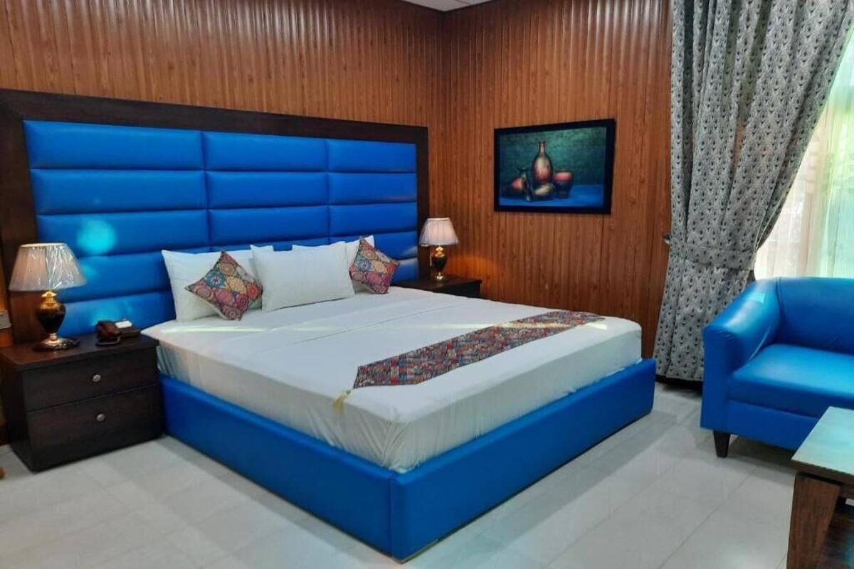 A bedroom with a large bed, wooden panel walls, a painting, and a blue chair.