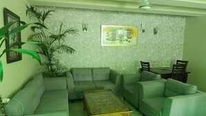 A living room with a sofa set, a coffee table, a dining table with chairs, and a large plant. - Royal Motel Executive (Islamabad)